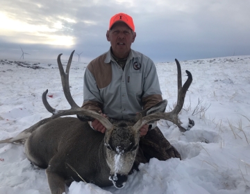 A hunter posing in the snow with his mule deer trophy